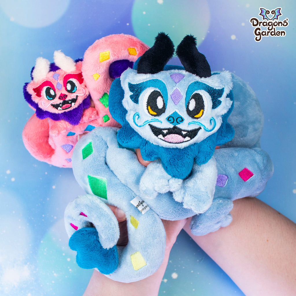 purple body with pink sakura cherry blossom snake plushie on a sparkly blue background being held with one hand